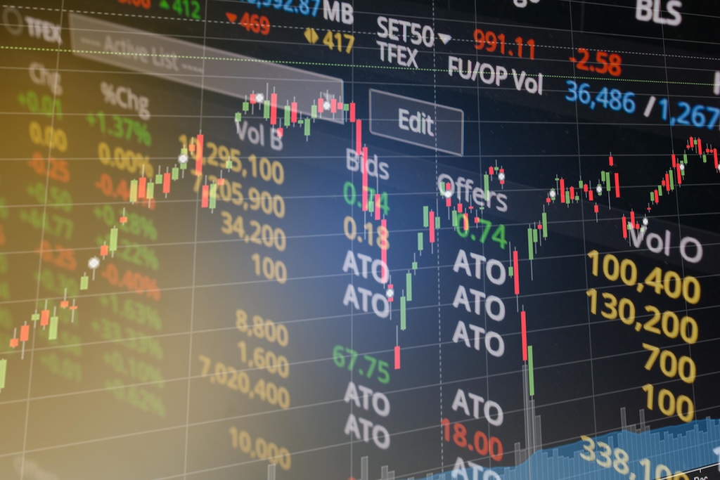 株価のローソク足チャートと板情報（Bids/Offers）が映し出されたデジタルの取引画面。赤と緑のローソク足が複雑な値動きを示し、その周囲には取引量や気配値などの数値データが並んでいる。画面左下から差し込む柔らかな光のフレアが、テクニカルでモダンな雰囲気を演出している。